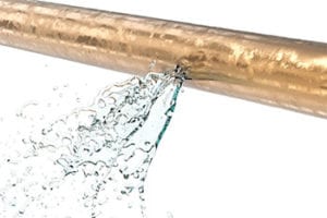Leaking copper pipe with water spraying out, illustrating the importance of immediate plumbing repairs for damaged pipes.
